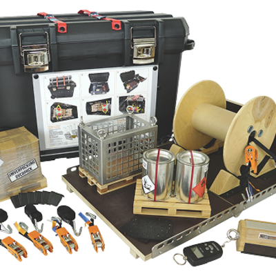 Verschiedene Trainingsgeräte und -ausrüstungen, darunter ein schwarzer Koffer, eine Drahtspule, Metallkanister, ein Metallkäfig, Gurte, Holzblöcke, Fernbedienungen und ein Anleitungsdiagramm, alles auf einer weißen Fläche angeordnet.